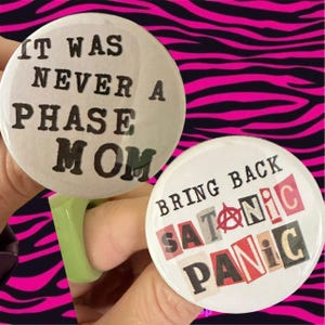 May include: Two white button pins with black text. The first pin says "It was never a phase mom". The second pin says "Bring back satanic panic" in red, black, and white letters.