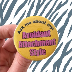 May include: Yellow button with the text "Ask me about my: Avoidant Attachment Style" in black and pink lettering.
