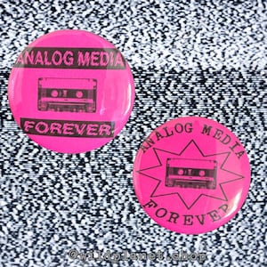 May include: Two pink circular buttons with black text and a cassette tape graphic. One button reads "ANALOG MEDIA FOREVER" in a rectangular layout. The other has the same text in a starburst design.