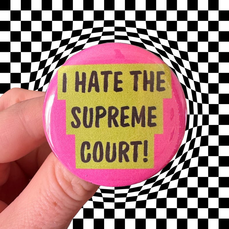Peut inclure: Un bouton rond rose avec le texte "I HATE THE SUPREME COURT!" en lettres noires sur un fond jaune. Le bouton est pr&eacute;sent&eacute; sur un fond &agrave; carreaux noir et blanc d&eacute;form&eacute;.