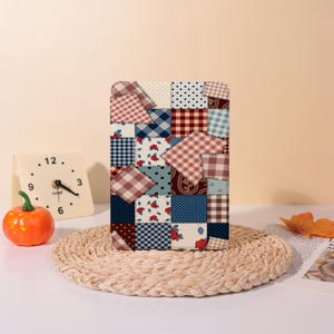 May include: A rectangular patchwork design with squares of diverse patterns and colours, including gingham, polka dots, and floral prints. The design is mainly in shades of red, blue, and cream. The patchwork is displayed on a light-coloured surface.