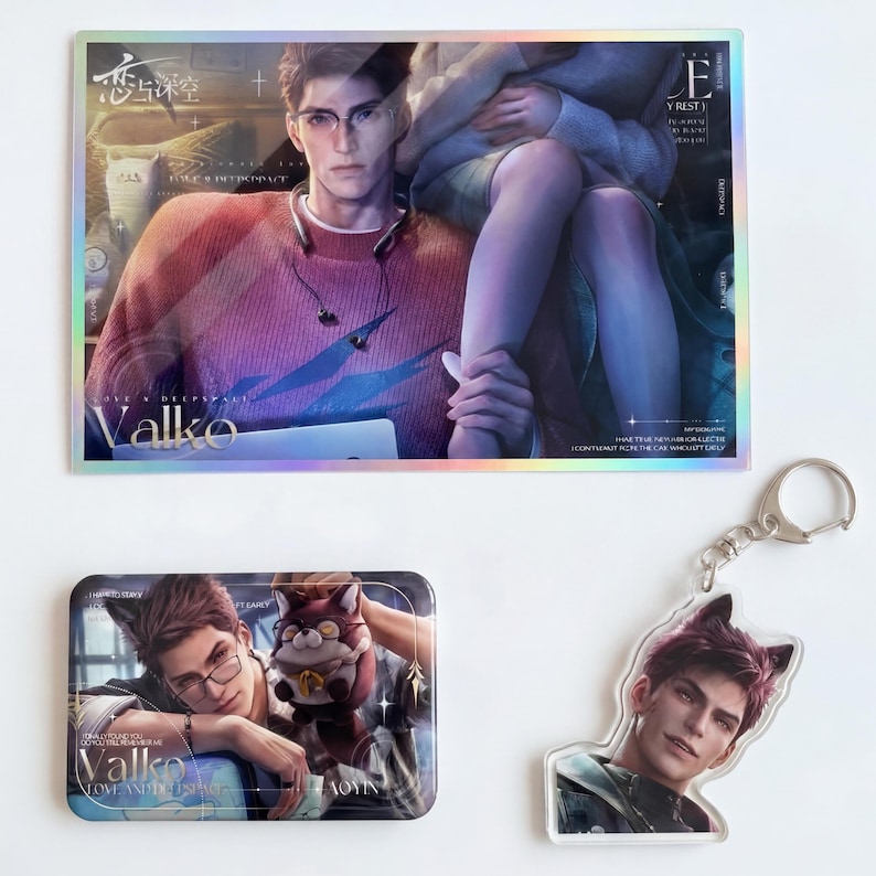 May include: A rectangular holographic print featuring a male character in a red sweater, a smaller rectangular tin with an illustration of a character with cat ears, and a clear acrylic keychain of a character with cat ears and dark hair.