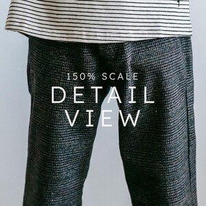 May include: Close-up of gray and black patterned pants with the text "150% SCALE DETAIL VIEW" in white. The pants are paired with a striped black and white top. The image focuses on the texture and detail of the clothing.