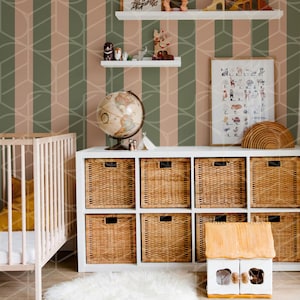 May include: A white crib with a yellow blanket, a white shelf with a globe, toys, and a framed alphabet chart, a white shelf with a framed picture and a doll, a white cabinet with wicker baskets, and a white rug in front of a green and pink striped wallpaper.