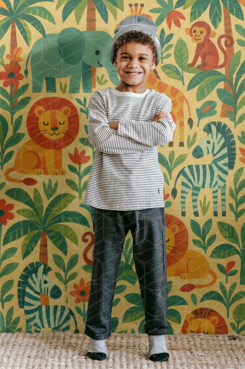May include: A child wearing a striped long-sleeve shirt, gray patterned pants, and a gray beanie smiles in front of a jungle-themed wallpaper. The wallpaper features illustrations of animals like lions, zebras, and elephants.