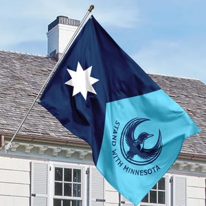 May include: A flag with a navy blue and light blue design. The navy blue section features a white eight-pointed star. The light blue section has a circular emblem with a loon and the text "STAND WITH MINNESOTA".
