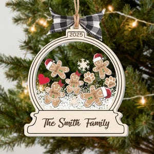 May include: Wooden Christmas ornament shaped like a snow globe, featuring gingerbread people with Santa hats and family names. Includes a black and white checkered bow and the year 2025. The text "The Smith Family" is at the bottom.