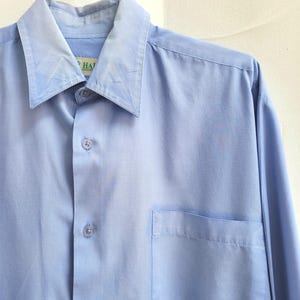 May include: A light blue button-down shirt with a pointed collar and a chest pocket. The long-sleeved shirt is hanging on a metal hanger. The shirt has a classic design.