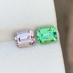 Può includere: Due gemme rettangolari, una rosa chiaro e l'altra verde brillante. Entrambe hanno un taglio sfaccettato e sono esposte su una superficie bianca. Queste gemme sono probabilmente per la creazione di gioielli.