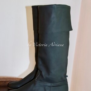 May include: A pair of dark green leather knee-high boots with a fold-over top. The boots have a low heel and a rounded toe.