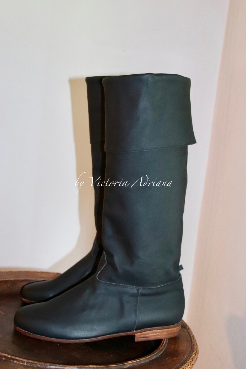 May include: A pair of dark green leather knee-high boots with a fold-over top. The boots have a low heel and a rounded toe.