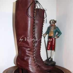 May include: A pair of brown leather knee-high boots with lace-up fronts and a chunky heel. The boots are on a wooden tray with a woven edge.