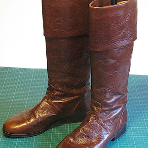 May include: A pair of brown leather knee-high boots with a fold-over top. The boots have a pointed toe and a low heel.
