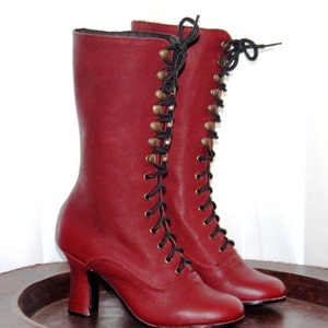 May include: A pair of burgundy leather lace-up boots with black laces and gold-toned eyelets. The boots have a high heel and a rounded toe.