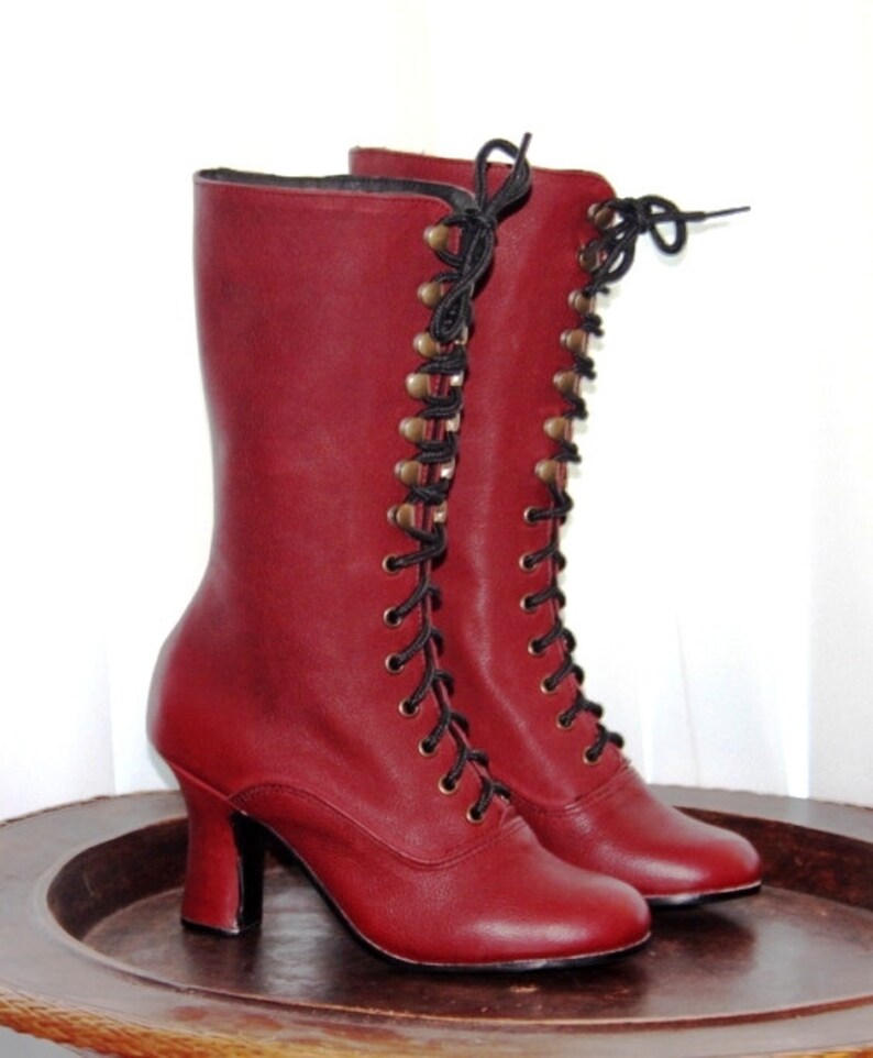 May include: A pair of burgundy leather lace-up boots with black laces and gold-toned eyelets. The boots have a high heel and a rounded toe.