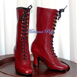 May include: A pair of red leather lace-up boots with black laces and gold-toned eyelets. The boots have a high heel and a rounded toe.