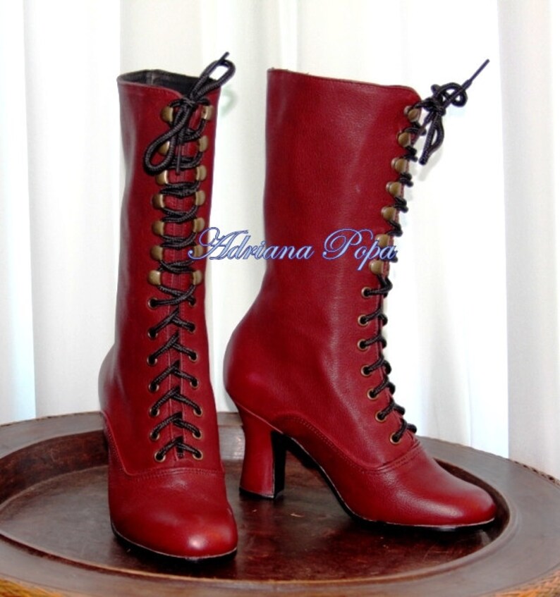 May include: A pair of red leather lace-up boots with black laces and gold-toned eyelets. The boots have a high heel and a rounded toe.