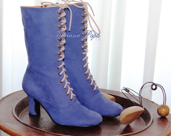 May include: A pair of blue suede lace-up boots with brown metal eyelets and a high heel. The boots are on a wooden surface.