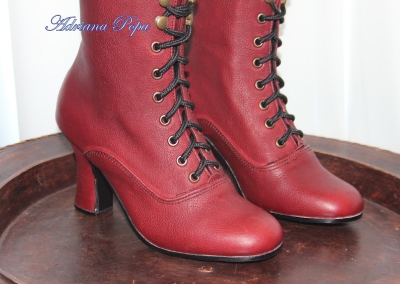 May include: A pair of burgundy leather ankle boots with black laces and gold eyelets. The boots have a high heel and a pointed toe.