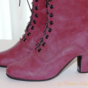 May include: A pair of burgundy-colored ankle boots with black laces and small heels. The boots have a vintage style, with a lace-up design and a rounded toe. The boots are made of a textured material.
