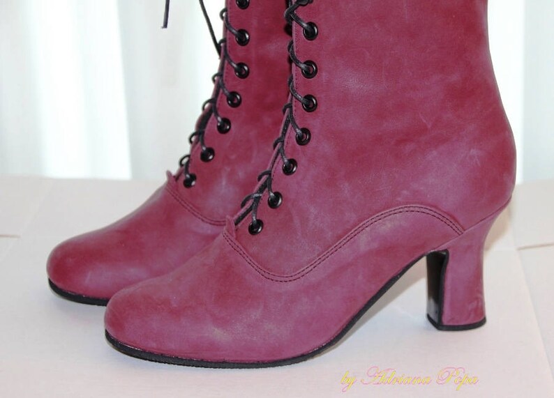 May include: A pair of burgundy-colored ankle boots with black laces and small heels. The boots have a vintage style, with a lace-up design and a rounded toe. The boots are made of a textured material.