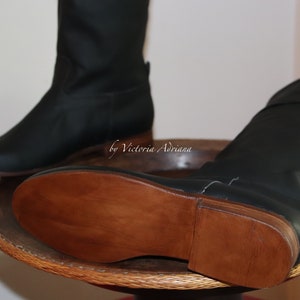 May include: A pair of black leather boots with brown wooden soles. The boots are on a wooden surface with a woven pattern.