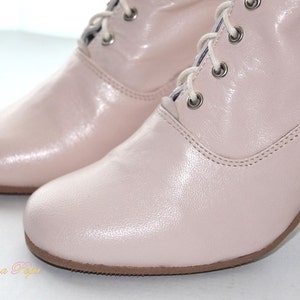 May include: A pair of light pink leather ankle boots with lace-up closures. The boots have a low block heel and a rounded toe.