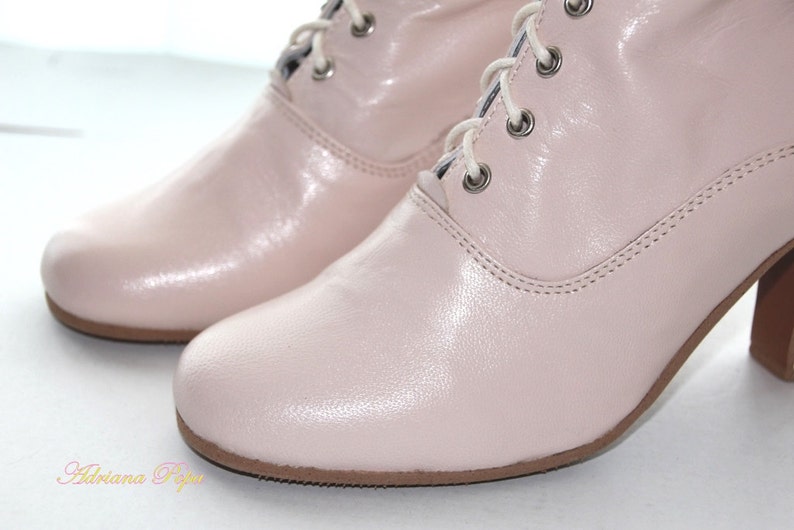 May include: A pair of light pink leather ankle boots with lace-up closures. The boots have a low block heel and a rounded toe.