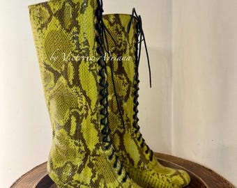 May include: Green snake-skin patterned lace-up boots with a block heel. The boots are on a wooden surface.