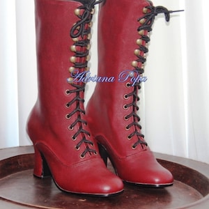 May include: A pair of burgundy leather lace-up boots with black laces and gold-toned eyelets. The boots have a high heel and a rounded toe.