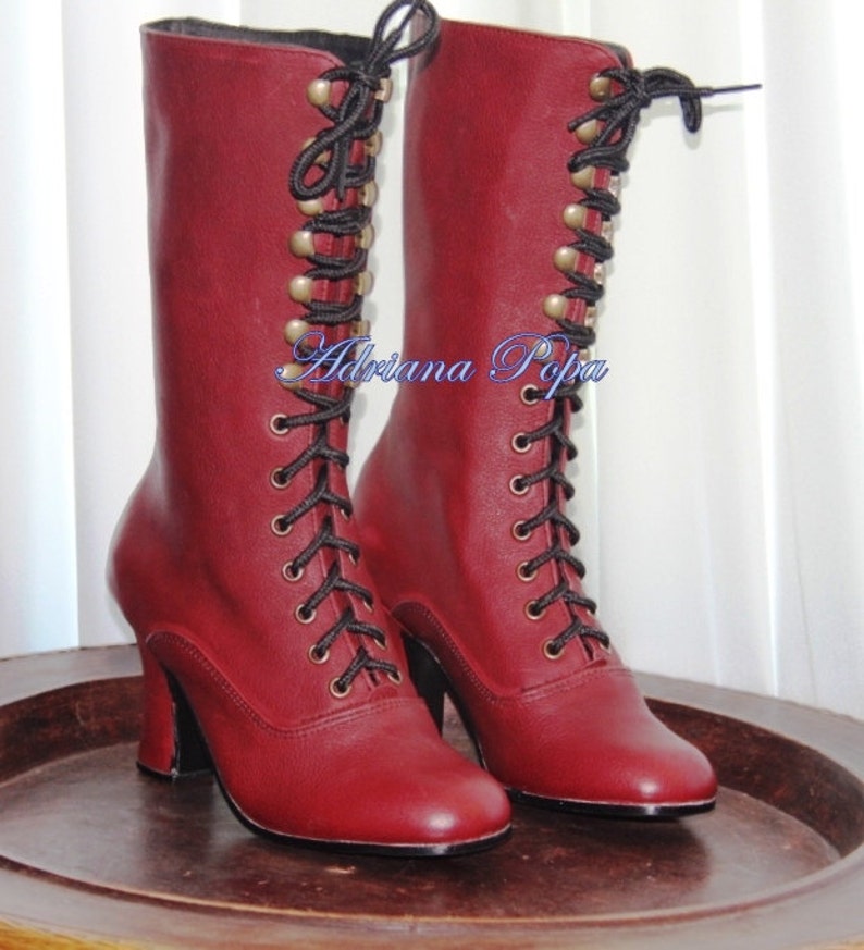 May include: A pair of burgundy leather lace-up boots with black laces and gold-toned eyelets. The boots have a high heel and a rounded toe.