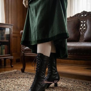 May include: A pair of black leather lace-up boots with a mid-calf height and a low block heel, worn with beige ribbed tights under a dark green skirt. The boots feature thin black laces and metal eyelets, with the text Adriana Popa visible.