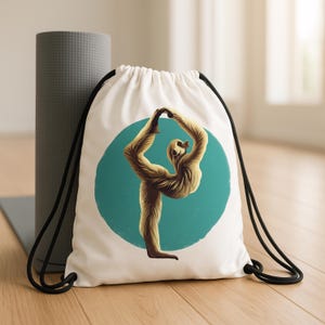 May include: White drawstring bag featuring a tan-colored illustration of a figure in a yoga pose against a teal circle. The bag has black drawstrings and is next to a gray yoga mat and rolled-up exercise mat.
