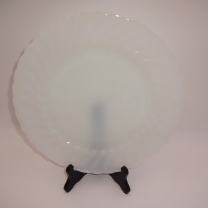 Puede incluir: Un plato blanco opaco redondo con un borde festoneado. El plato está en un soporte negro.