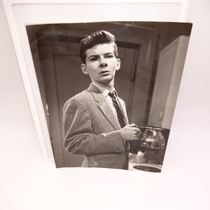 Puede incluir: Una fotografía en blanco y negro de un joven con chaqueta de traje y corbata, sosteniendo una cafetera.