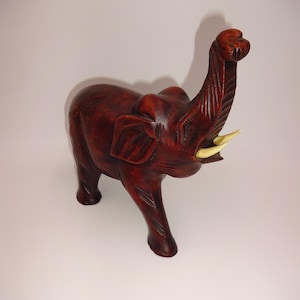 May include: A dark brown wooden elephant figurine with its trunk raised in the air. The elephant has ivory-coloured tusks.