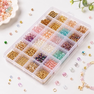 May include: A clear plastic storage container with eighteen compartments filled with an assortment of colourful beads, including metallic gold, iridescent, clear, pink, purple, and teal options, along with small gold metal jump rings.