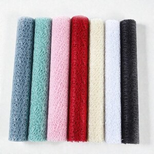 May include: Seven rolls of decorative mesh fabric in various colors, including blue, green, pink, red, cream, white, and black. The mesh has a textured, open weave pattern. The rolls are tightly wound and displayed vertically.