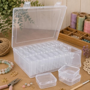 May include: A clear plastic storage container with a hinged lid, featuring multiple small, removable individual compartments inside. The rectangular organizer is designed for sorting small items and includes several separate square boxes.