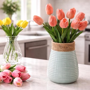 Peut inclure: Un vase bleu clair avec une bande tressée sur le dessus contient un bouquet de tulipes pêche. Un autre vase en verre transparent expose des tulipes jaunes. Des tulipes roses sont éparpillées.
