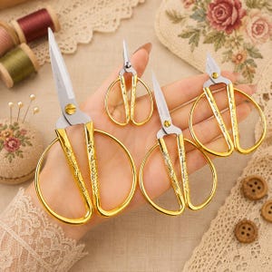 May include: A set of four stainless steel scissors with gold-toned handles featuring an embossed floral pattern. The scissors vary in size, with two larger pairs and two smaller pairs, all featuring a central gold screw and sharp metal blades.