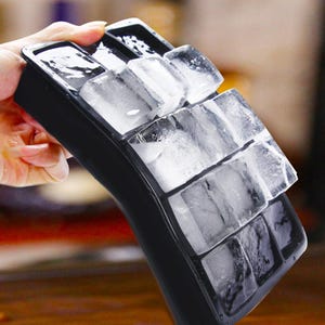 Könnte beinhalten: Eine schwarze Eiswürfelschale gefüllt mit klaren, rechteckigen Eiswürfeln. Die Schale wird in einem Winkel gehalten, wodurch die Würfel zur Geltung kommen. Die Eiswürfel sind teilweise geschmolzen, mit sichtbaren Wassertröpfchen. Die Schale besteht aus flexiblem Material.