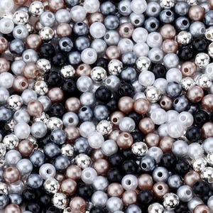 May include: A close-up shot of a collection of beads in various colors. The beads are a mix of pearlized white, silver, black, gray, and bronze. The beads are round with a hole through the center, and are scattered randomly.