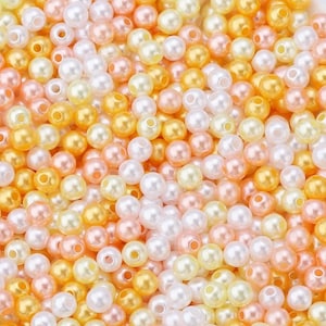 May include: A close-up view of a pile of small, round beads in various colors. The beads are a mix of white, peach, yellow, and gold, creating a warm and inviting palette. These beads are likely used for jewelry making or other craft projects.