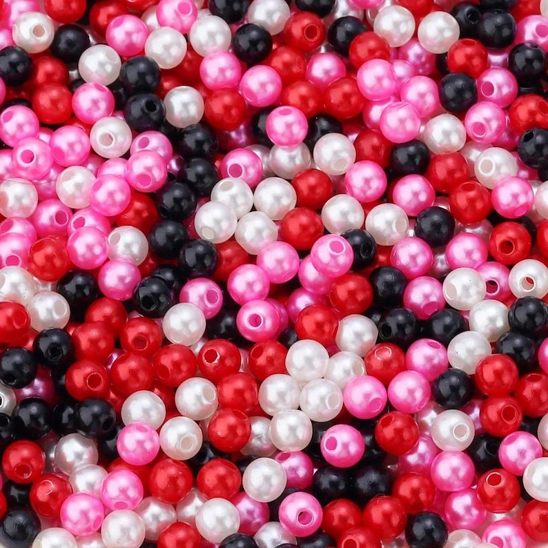 May include: A close-up shot of a pile of small, round beads in various colors. The beads are a mix of red, pink, black, and white, creating a vibrant and textured surface. The beads appear to be made of a glossy material.