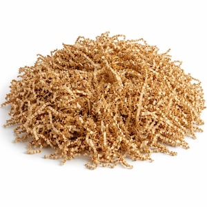 Può includere: Un mucchio di materiale di imballaggio in carta marrone sminuzzata. La carta è tagliata in sottili strisce arricciate, creando un aspetto strutturato e voluminoso. Il materiale viene probabilmente utilizzato per l'ammortizzazione e la protezione degli articoli durante la spedizione o come riempitivo decorativo.