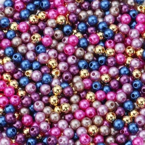 May include: A collection of colorful beads in shades of pink, blue, purple, and gold. The beads are round with a hole through the center, suitable for jewelry making or crafts. The beads are scattered, creating a textured surface.