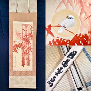 May include: A vertical hanging scroll featuring a painting of a white bird perched on a branch amidst red bamboo stalks against a pale background. The scroll includes a wooden storage box with black Japanese calligraphy characters written on the lid.