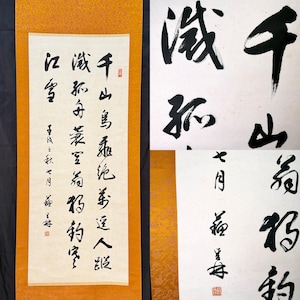 May include: A vertical hanging scroll featuring black ink calligraphy on a cream-colored paper background. The scroll is framed by a textured, mustard-yellow fabric border. The calligraphy consists of multiple columns of traditional characters.