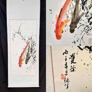 May include: A vertical wall scroll featuring a traditional ink and watercolor painting of two koi fish, one orange and one dark gray, swimming among black ink reeds. The artwork includes green paint splatters and black calligraphy text with a red seal.